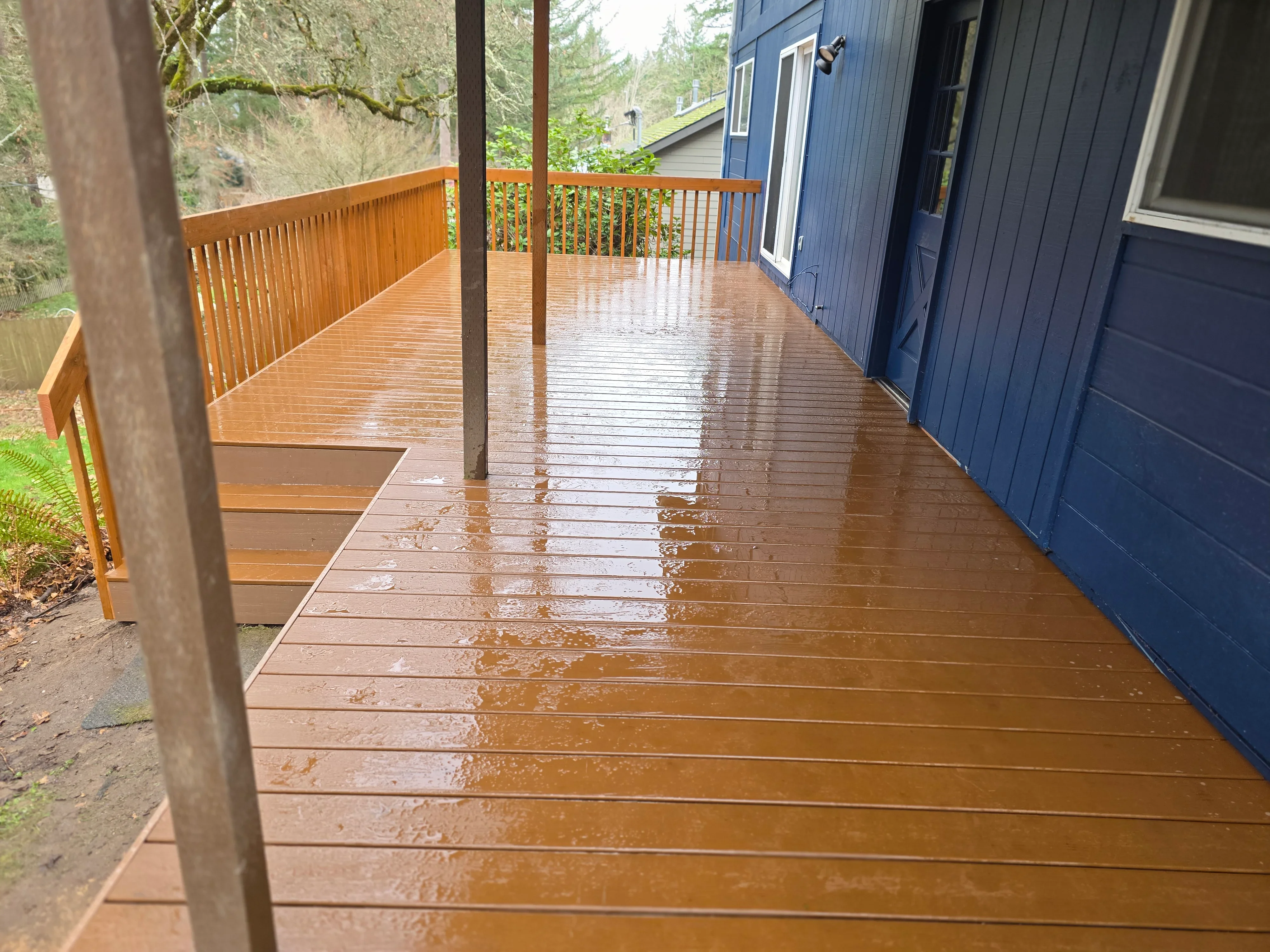 Composite deck with brown boards, metal posts, and cable railings adjacent to blue house