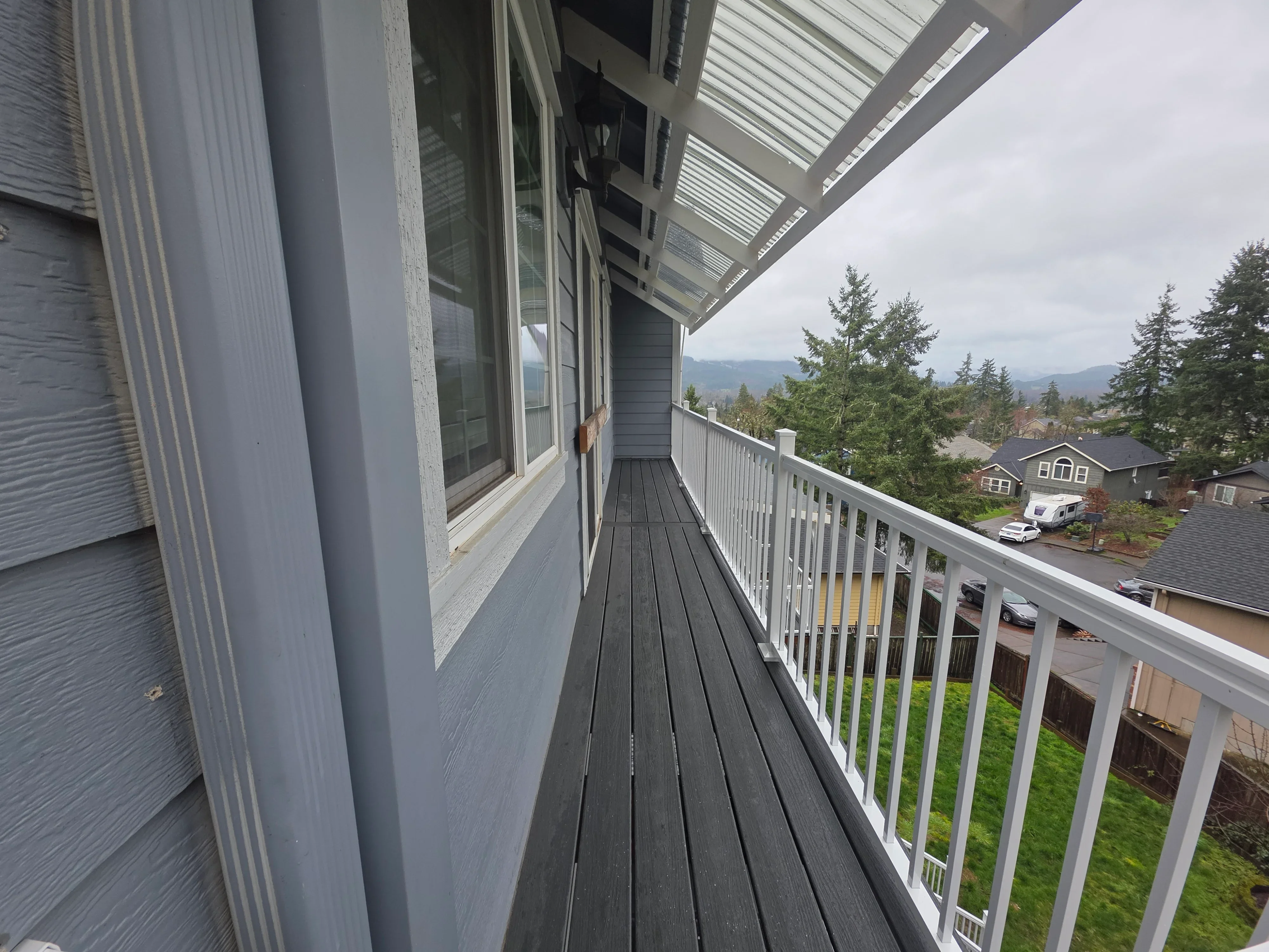 Dark composite deck with white metal railing and polycarbonate roof overhang overlooking residential neighborhood