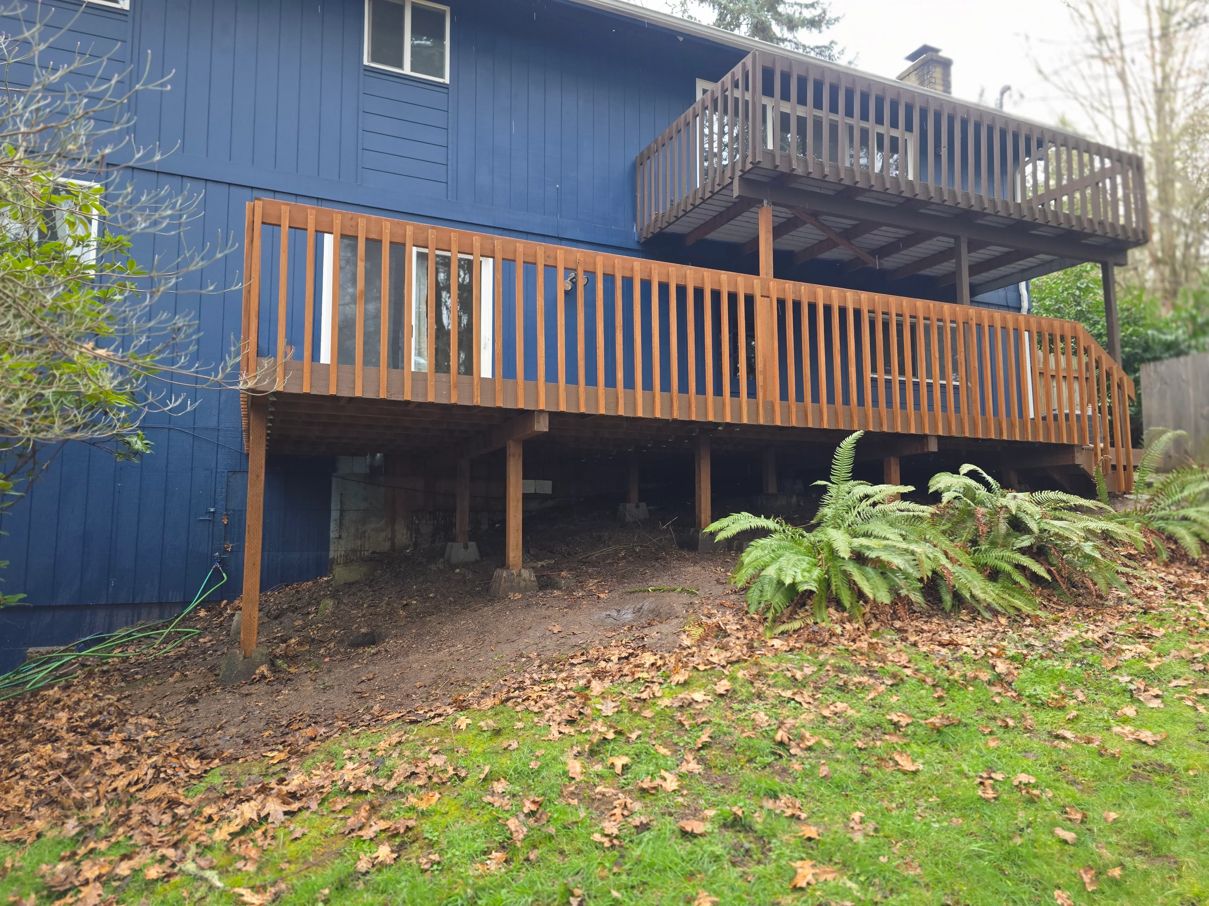 Two-level wooden deck with vertical and horizontal railings attached to blue house