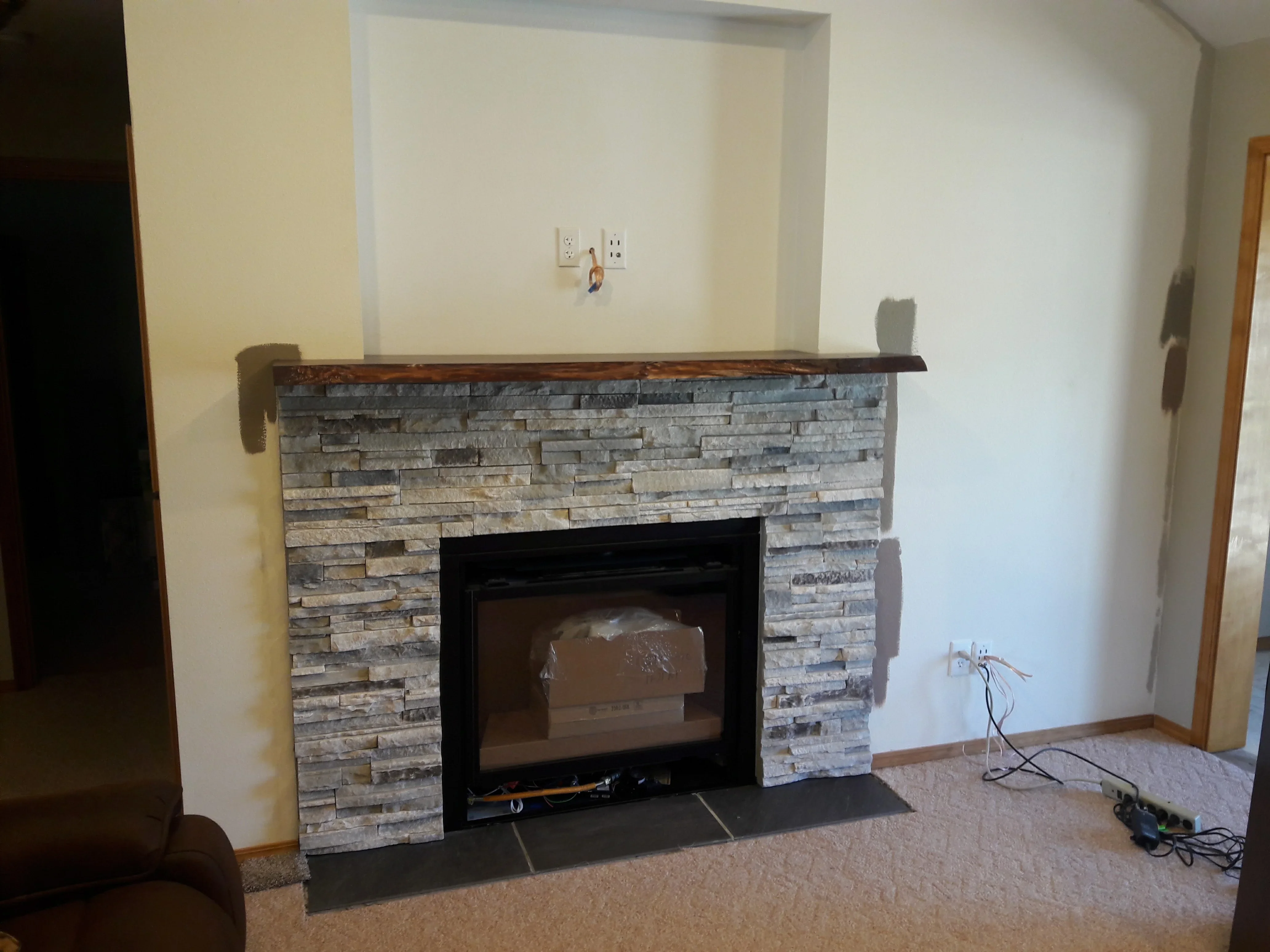 Stacked stone fireplace surround with black insert, wood mantel, and slate hearth