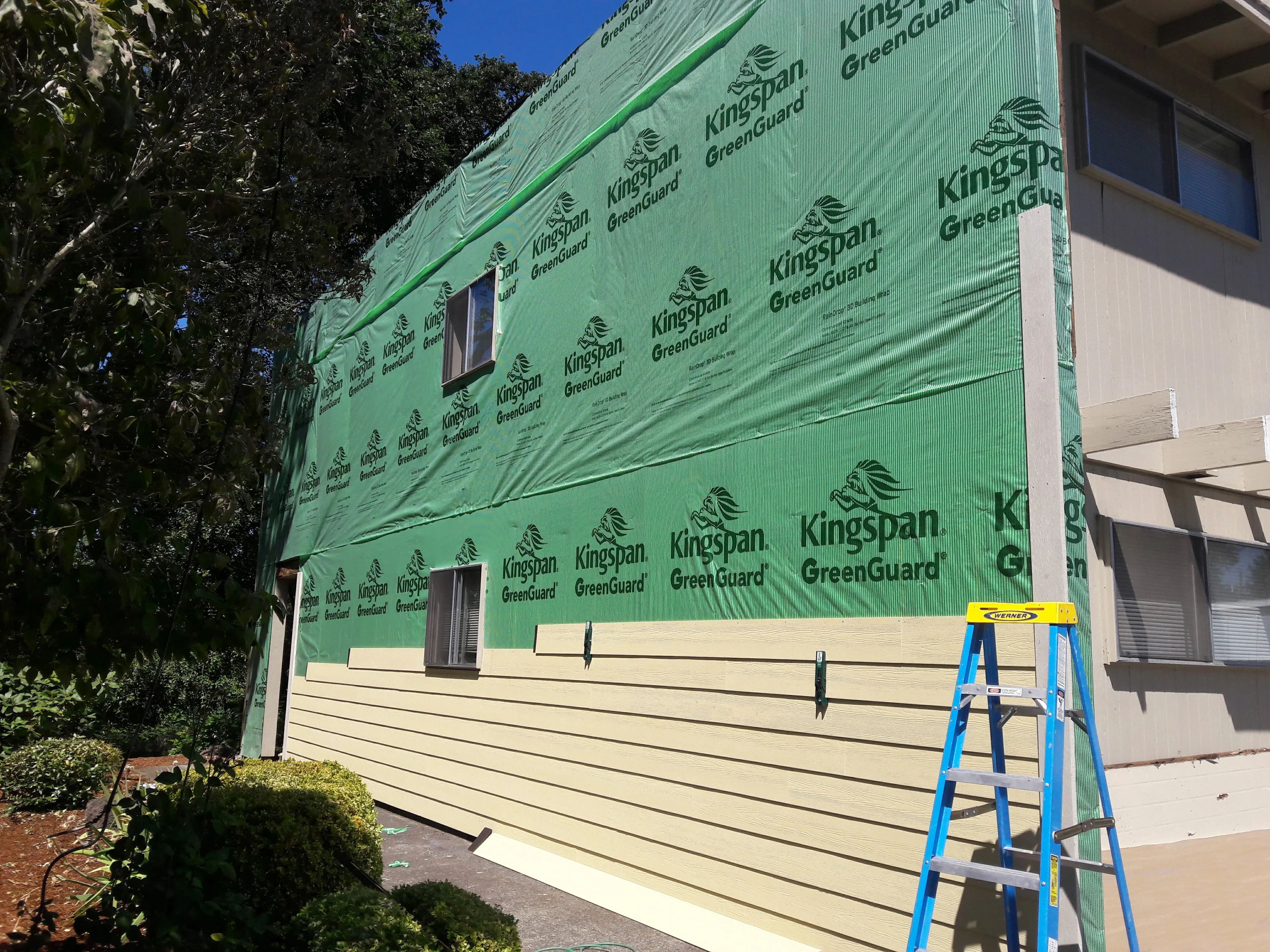 Cream horizontal lap siding with green weather barrier membrane and window flashing installation
