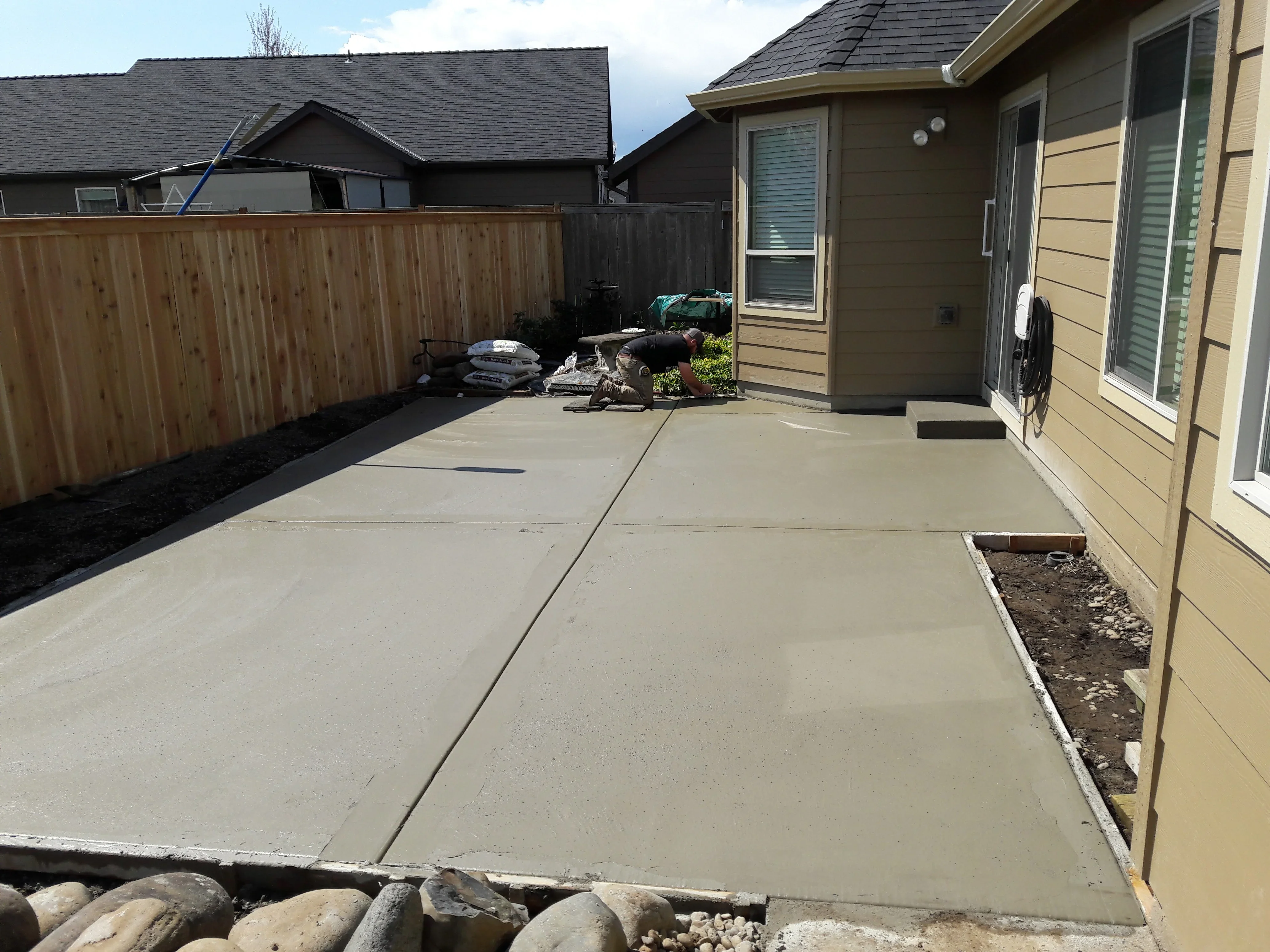 Finished concrete patio with control joints, wooden fence, and gravel base in residential backyard