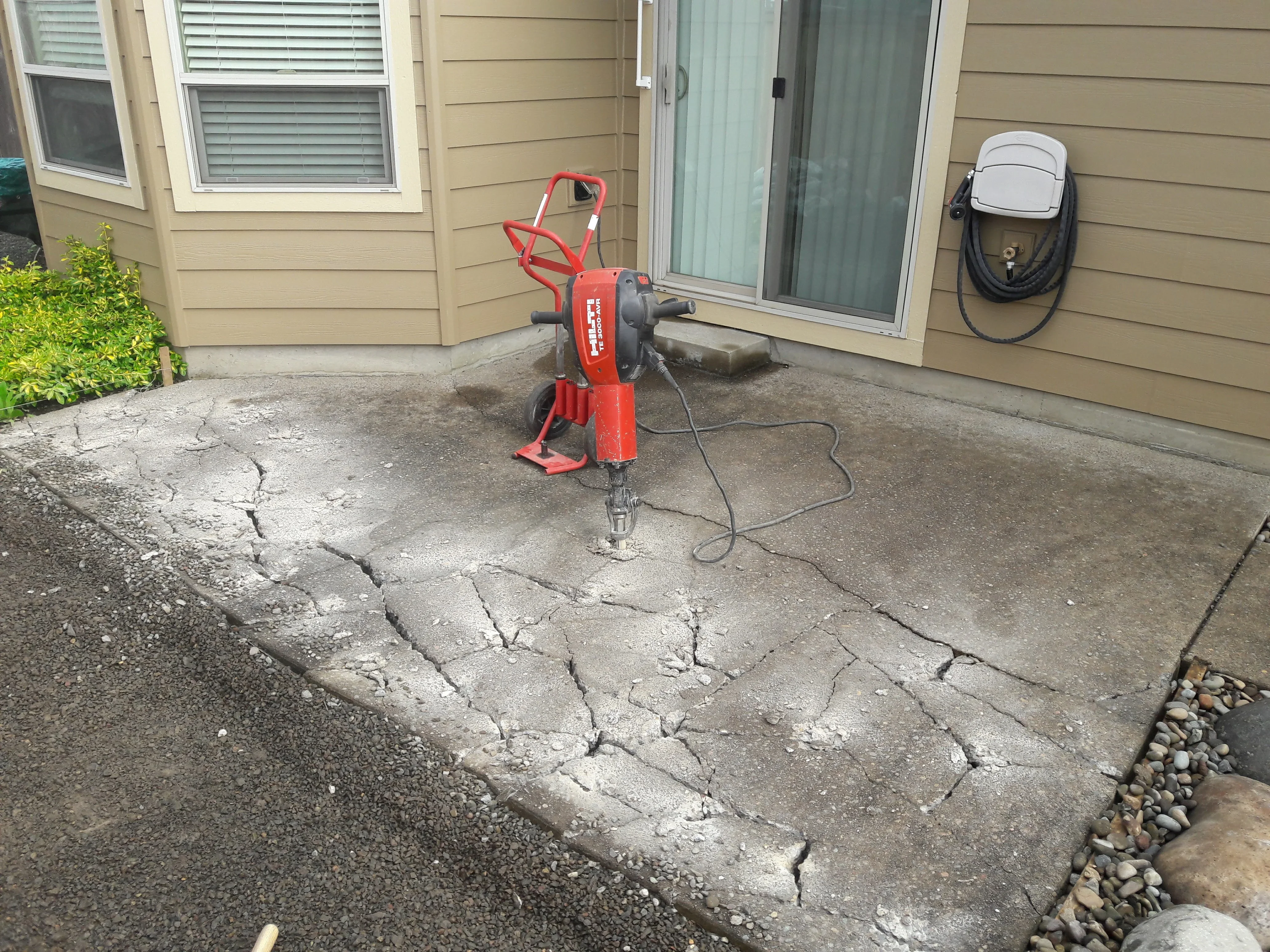 Red concrete cutting equipment on cracked patio surface with tan siding house in background