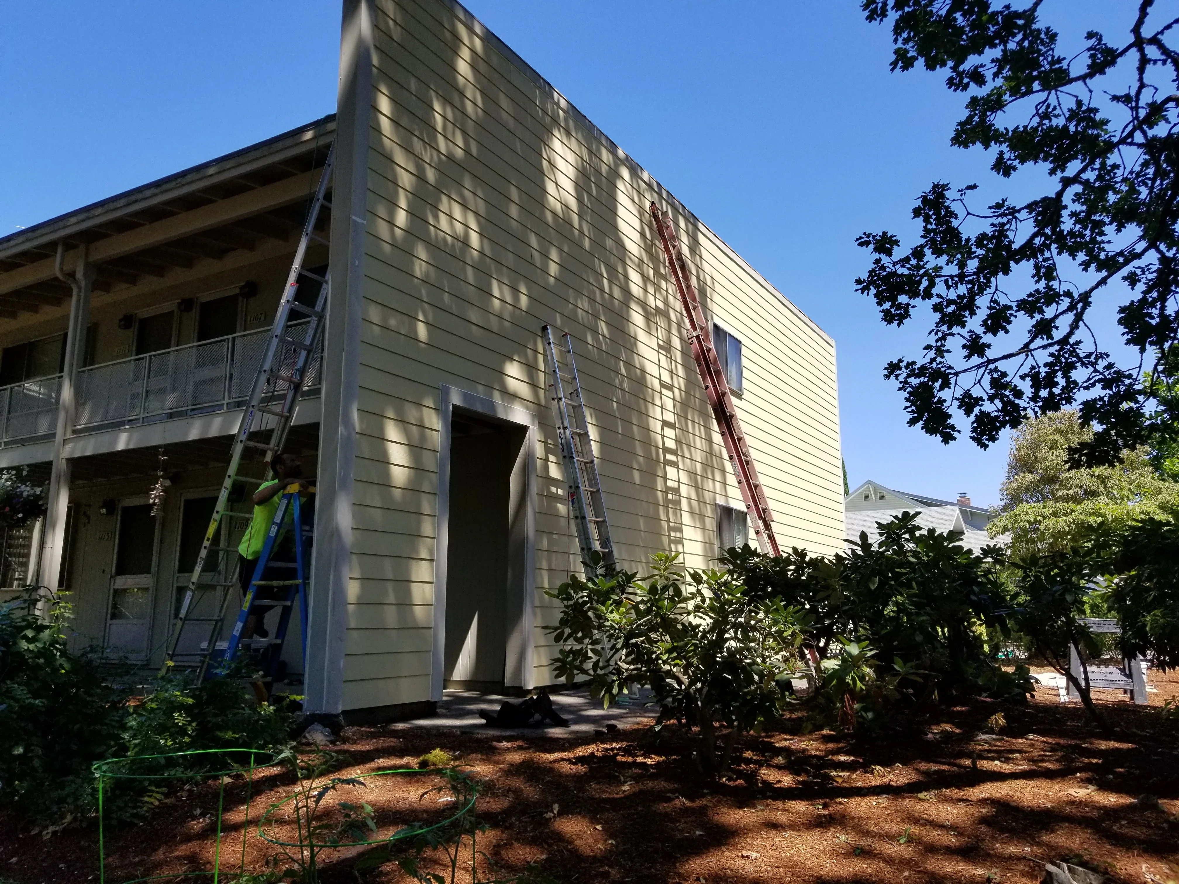 Horizontal fiber cement siding installation on residential home exterior with ladders and staging