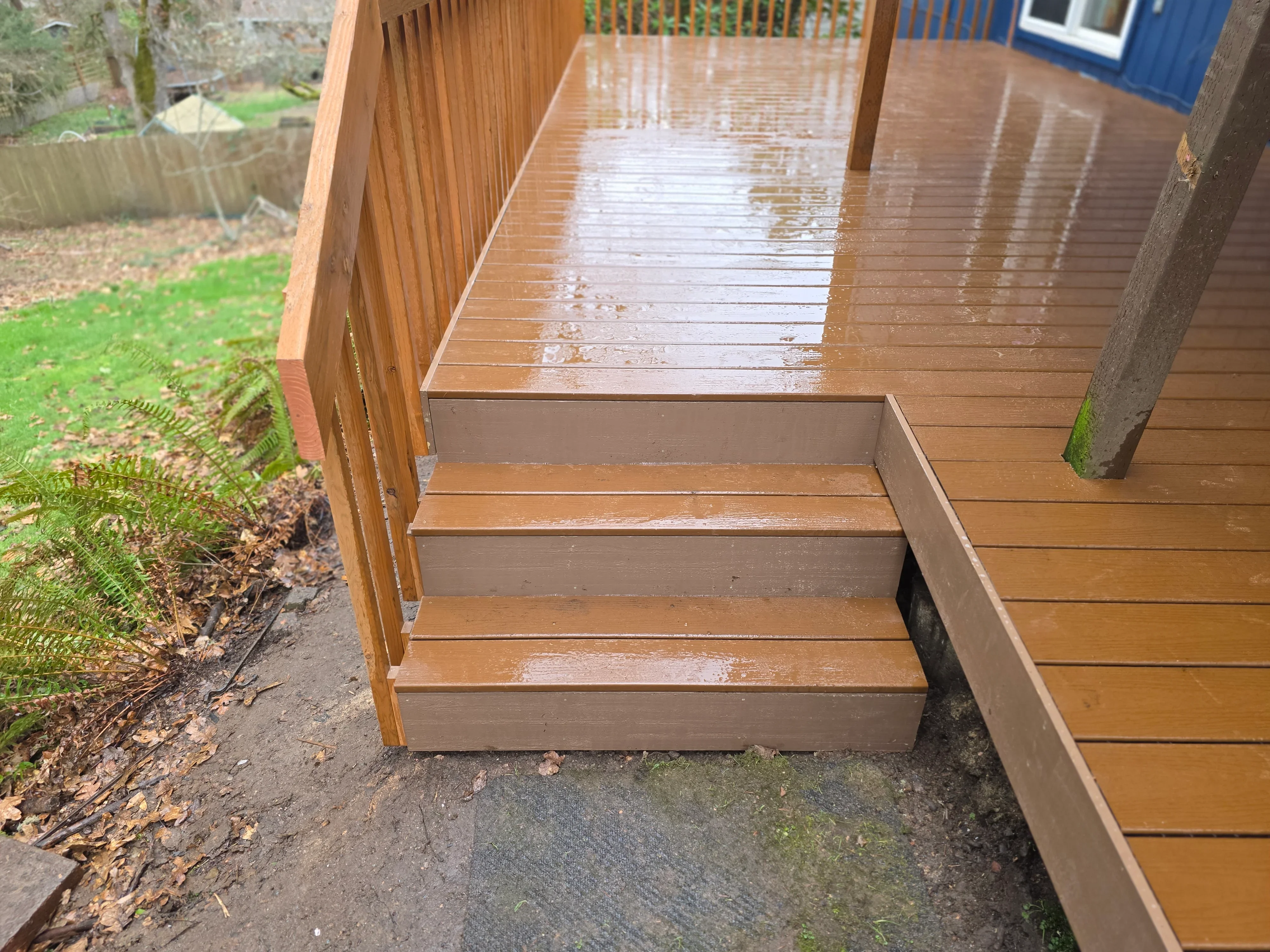 Composite deck with integrated stairs, vertical railings, and wet surface showing drainage
