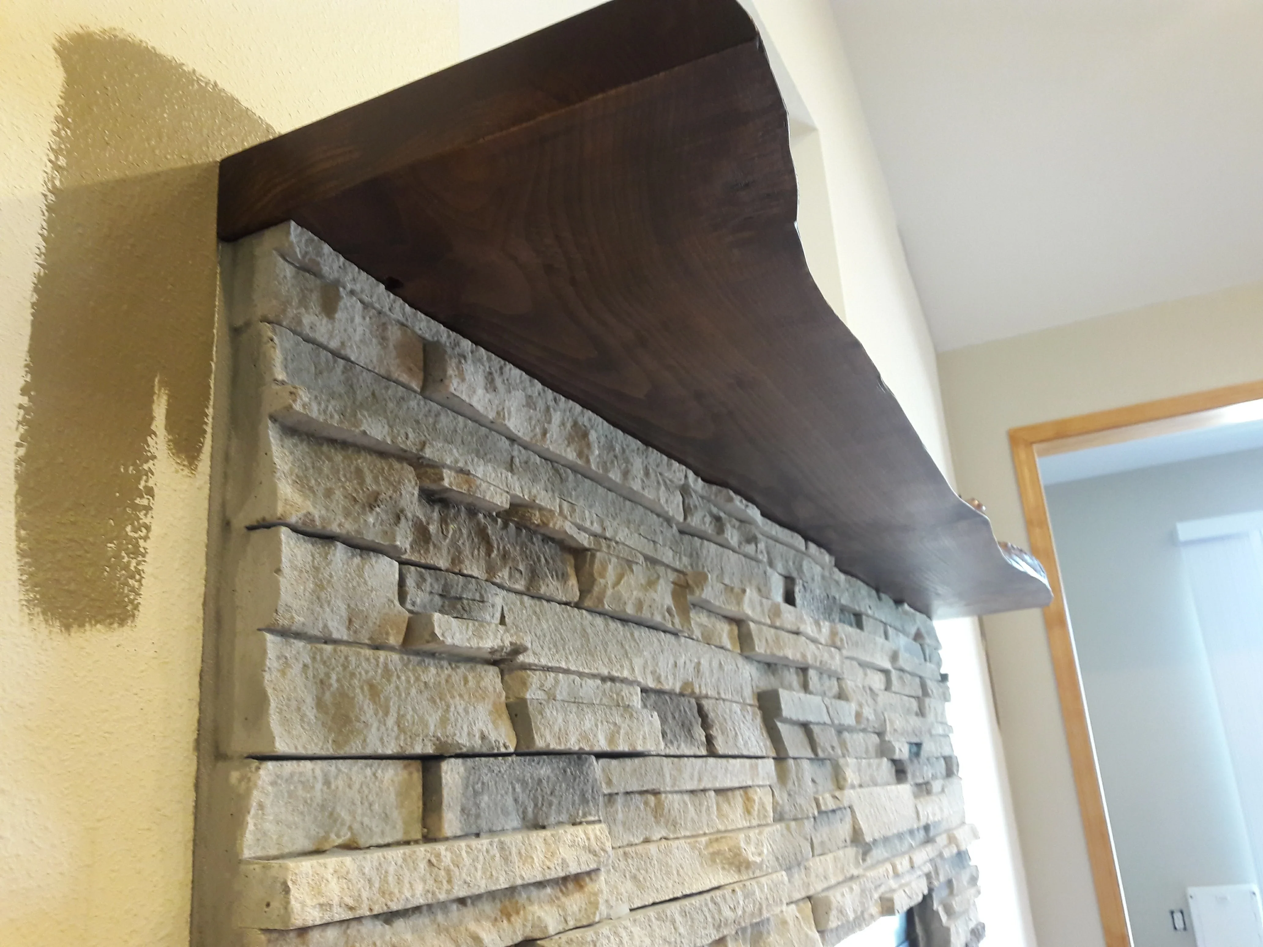 Stacked stone veneer accent wall with dark wood beam soffit and yellow drywall