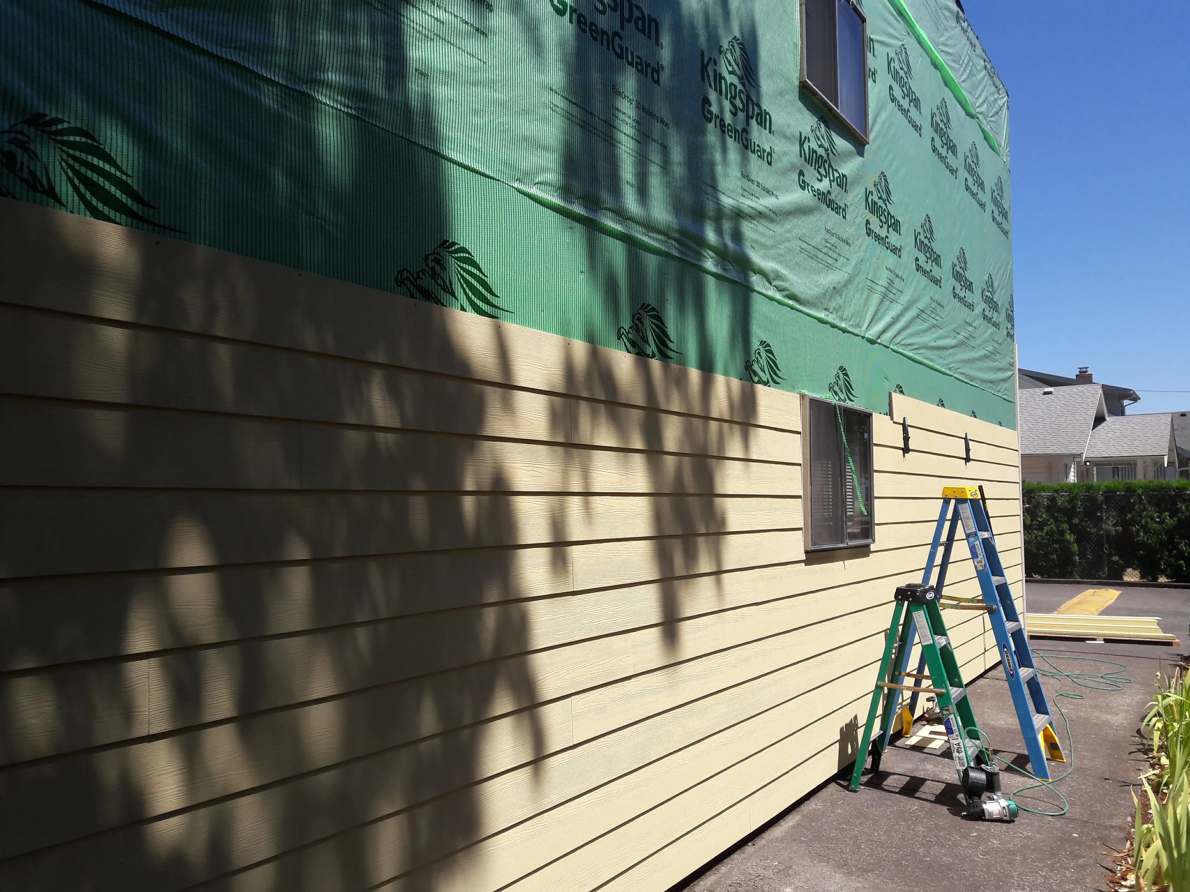 Cream-colored horizontal lap siding installation with green house wrap and weather barrier on residential exterior